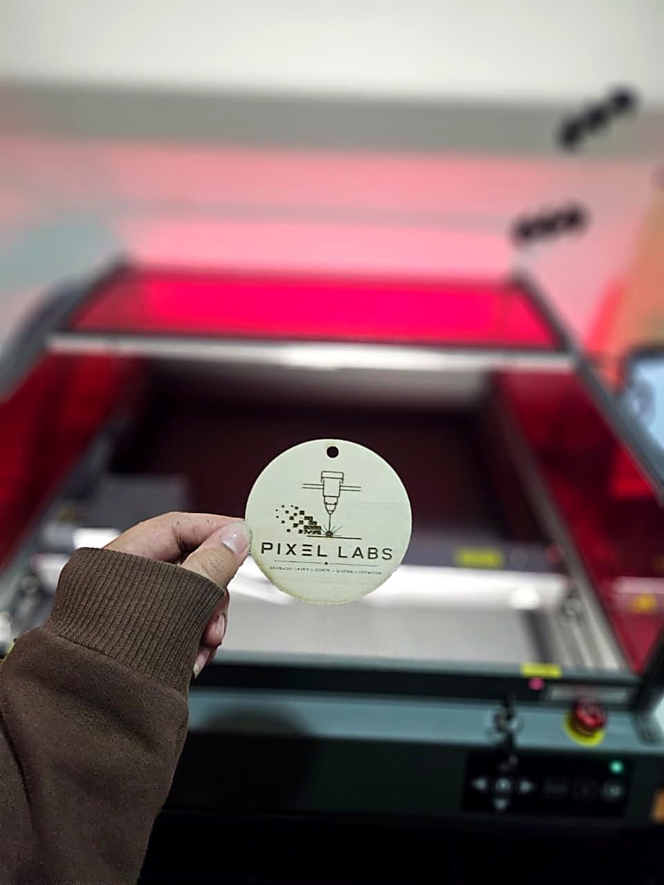 Pieza de madera grabada con el logo de Pixel Labs frente a la cortadora láser del taller en San Vicente